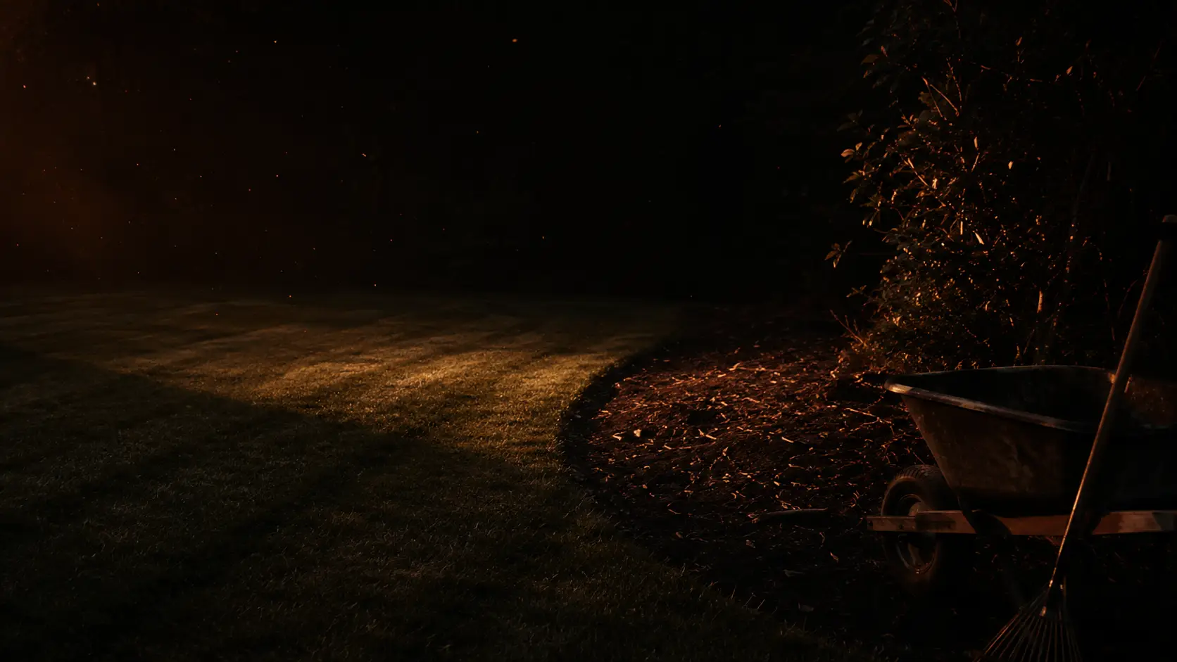 A freshly cut lawn with crisp mowing stripes at dusk, fresh mulch beds and a wheelbarrow at the edge of the property